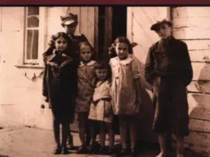 Sepia photo of children outside wooden house