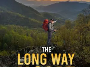 Hiker with backpack on mountain ridge at sunset