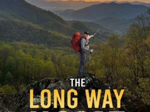 Hiker with backpack on mountain ridge at sunset